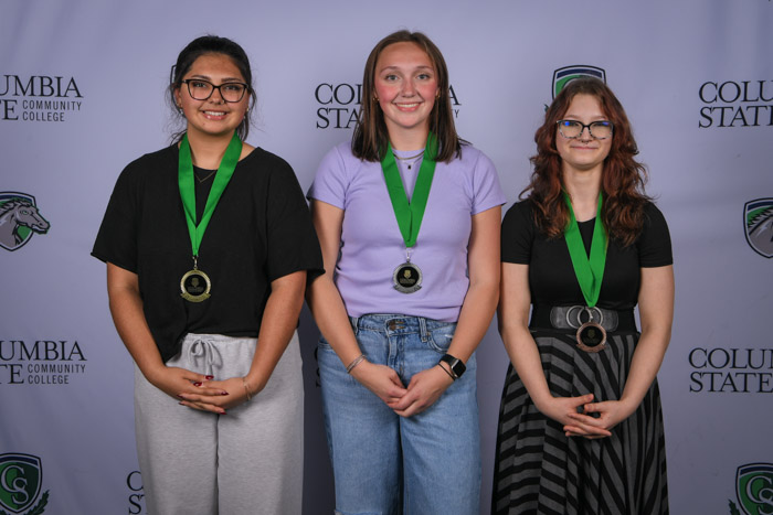 Photo shows a group of three people smiling at the camera with a white background featuring a repeated Columbia State logo pattern.