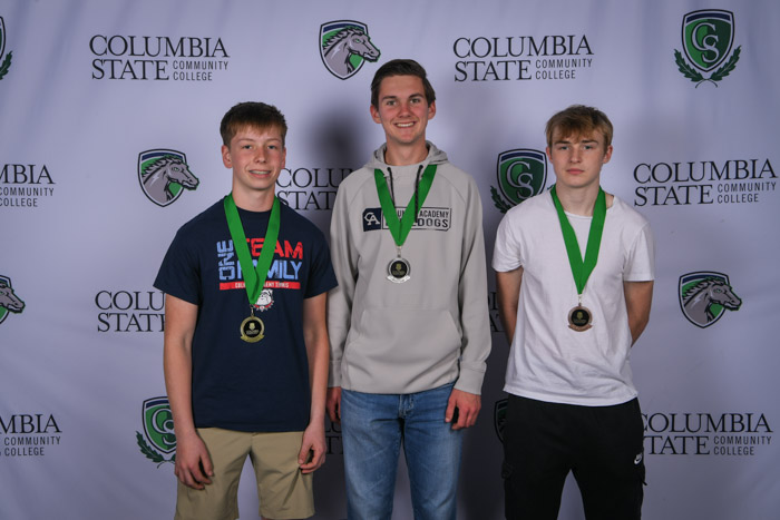 Photo shows a group of three people smiling at the camera with a white background featuring a repeated Columbia State logo pattern.