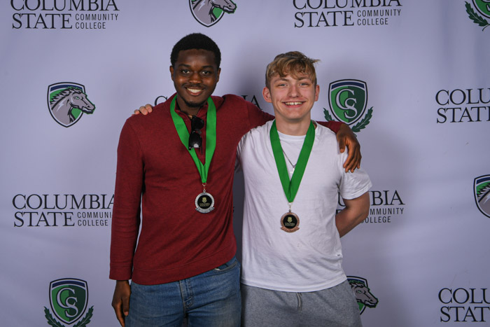 Photo shows a group of three people smiling at the camera with a white background featuring a repeated Columbia State logo pattern.