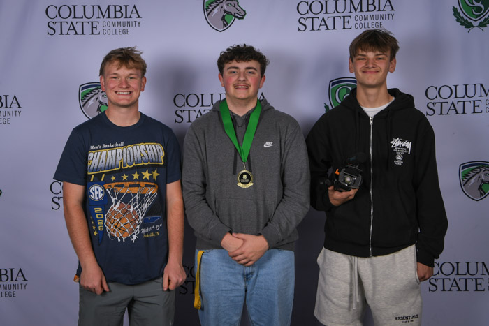 Photo shows a group of three people smiling at the camera with a white background featuring a repeated Columbia State logo pattern.