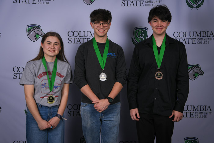Photo shows a group of three people smiling at the camera with a white background featuring a repeated Columbia State logo pattern.