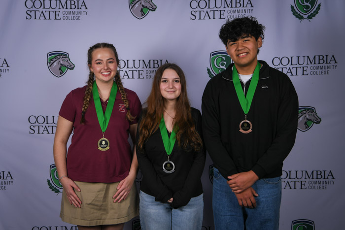 Photo shows a group of three people smiling at the camera with a white background featuring a repeated Columbia State logo pattern.
