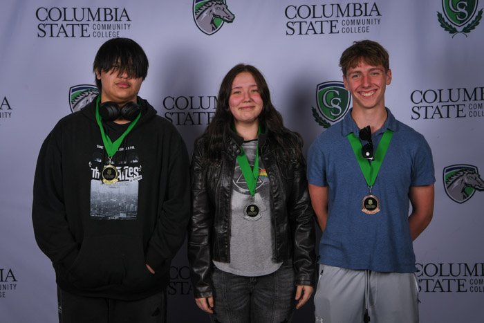 Photo shows a group of three people smiling at the camera with a white background featuring a repeated Columbia State logo pattern.
