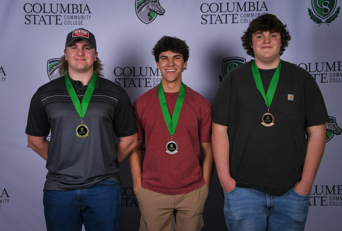 Photo shows a group of three people smiling at the camera with a white background featuring a repeated Columbia State logo pattern.
