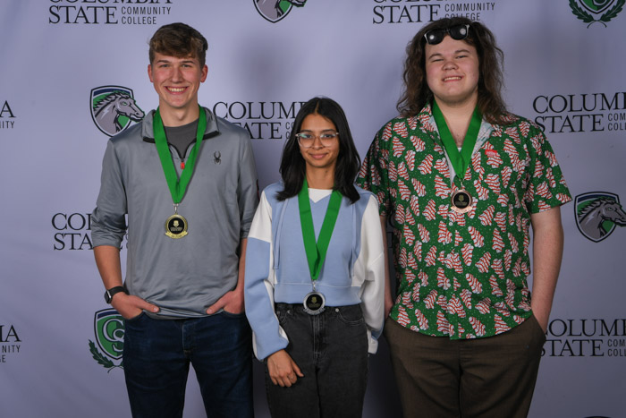 Photo shows a group of three people smiling at the camera with a white background featuring a repeated Columbia State logo pattern.