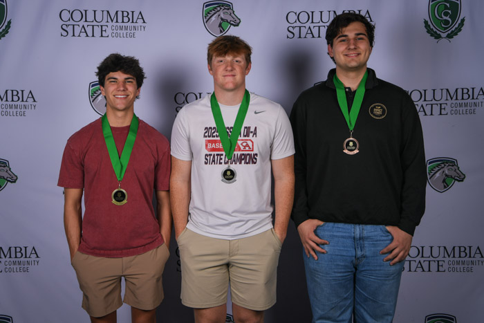 Photo shows a group of three people smiling at the camera with a white background featuring a repeated Columbia State logo pattern.