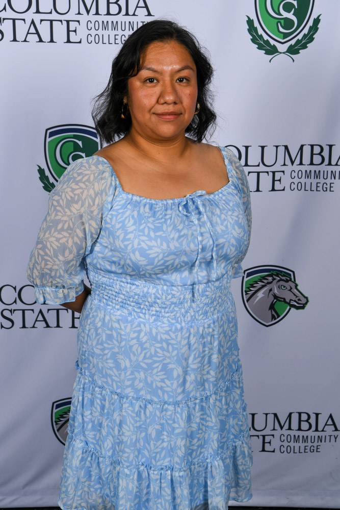 A woman stands in front of a white background.