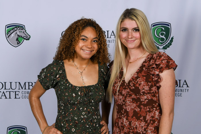 Two women stand in front of a white background.